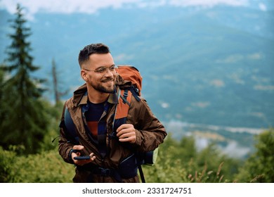 Happy hiker with smart phone walking up the hill during a rainy day. - Shutterstock ID 2331724751