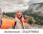 Happy hiker taking a selfie with victory gesture while enjoying the stunning mountain landscape