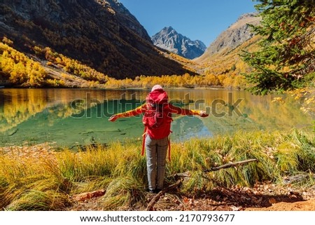 Happy hiker woman at lake in the autumnal mountains. Mountain lake and tourist with backpack
