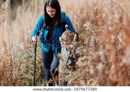 Happy hiking boy with trekking sticks in the mountains with his mother.