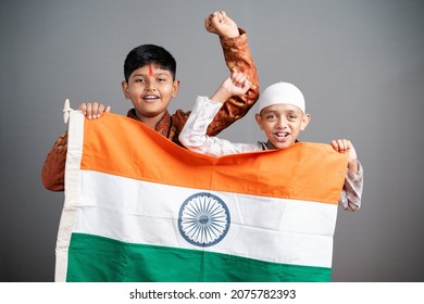 Happy Hindu Muslim Kids Shouting As India By Holding Indian Flag On Gray Background - Concept Of Independence Or Republic Day Celebrations, Unity In Diversity, Nationalism And Patriotism