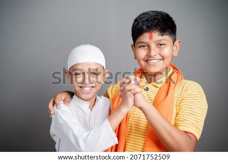 Happy Hindu Muslim kids showing unity by holding hands together by looking at camera on gray background - concept of diversity, bonding and multiethnic friendship