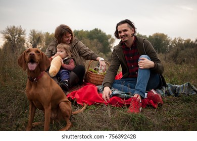 Happy Hipster Family With Little Child And Dog On A Picnic In Autumn Countryside Background.