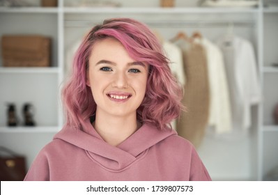 Happy Hipster Gen Z Teen Girl Fashion Designer, Stylist With Pink Hair And Piercing Wearing Hoodie Looking At Camera In Front Of Modern Clothes Wardrobe Closet, Face Head Shot Close Up Portrait.