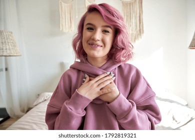 Happy hipster gen z teen girl blogger with smiling face with pink hair looking at camera recording live vlog channel, making video call, streaming on bed at home. Headshot portrait. Webcam view