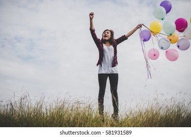 Happy hipster girl jumping with colorful toy balloons outdoors. Young woman having fun in green field against blue sky. Women freedom lifestyle concept.
