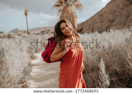  Happy hipster girl jumping and dancing with windy hair in desert nature holding a backpack. Young hipster traveler girl in gypsy look, in Coachella Valley in Southern California