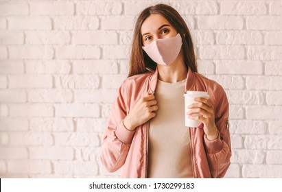 Happy hipster girl in stylish medical face mask and jacket drink coffee from paper cup. Beautiful trendy woman in pink protective face mask hold disposable cup of coffee or tea. Quarantine lifestyle - Powered by Shutterstock