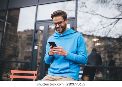 Happy Hipster-Typ in klassischen Spektakel für die Visualkorrektur mithilfe von Handy-Gadget für die Überprüfung der empfangenen E-Mail-Nachricht, lächelnd kaukasianischer Blogger auf Website in sozialen Medien surfen