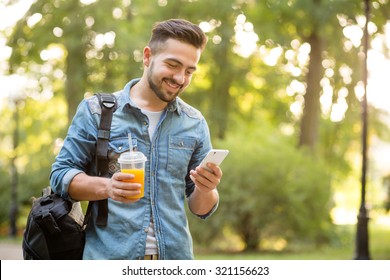 Happy hipster man walking in autumn park and smiling. Short-haited man looking at mobile phone's screen and enjoying reading messages. - Powered by Shutterstock