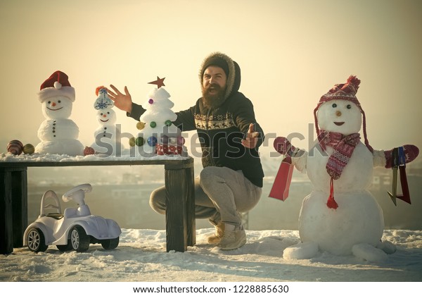 Happy\
hipster with open hands. Snowman with shopping bags on white sky.\
Snowy sculptures, xmas tree and gift box on wooden table. Toy car\
on snow. Christmas and new year presents\
concept.