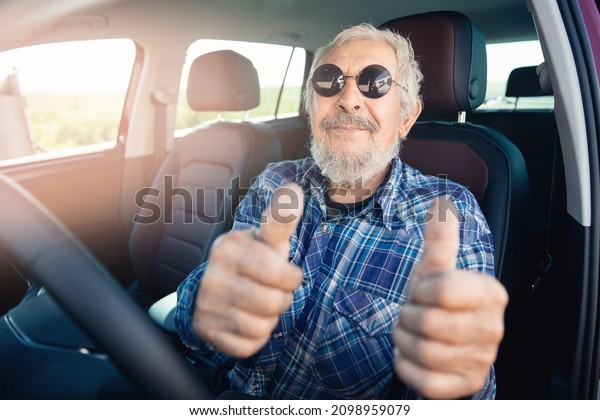 Happy hipster senior man pensioner smiling and\
driving car.