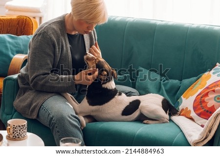 Happy hipster woman playing and bonding with her dog while relaxing on the couch at home. Love for pets concept. Pet loyalty and companionship.