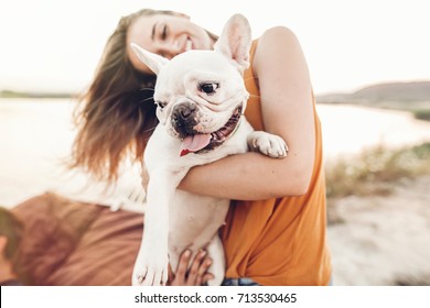 happy hipster woman playing with bulldog on the beach in sunset light, summer vacation. stylish girl with funny dog resting, hugging and having fun in sun, cute moments. space for text 