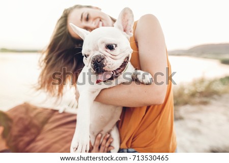 happy hipster woman playing with bulldog on the beach in sunset light, summer vacation. stylish girl with funny dog resting, hugging and having fun in sun, cute moments. space for text 