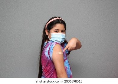 Happy Hispanic 10-year-old Girl With Mask Shows Her Arm That Just Received The Covid-19 Vaccine In The New Normal For The Pandemic
