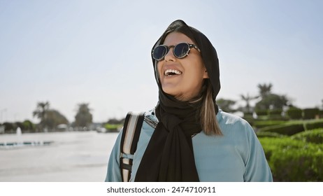 Happy hispanic adult woman wearing sunglasses and hijab at an islamic mosque in abu dhabi, uae, symbolizing tourism and cultural diversity. - Powered by Shutterstock