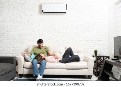 Happy Hispanic boyfriend and girlfriend relaxing on couch in living room at home while enjoying air conditioning