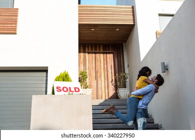 Happy Hispanic couple hugging in front of new house