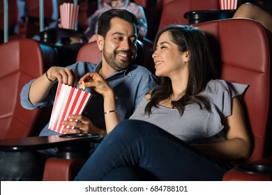 Happy Hispanic couple watching a movie at the cinema theater and sharing some popcorn - Powered by Shutterstock