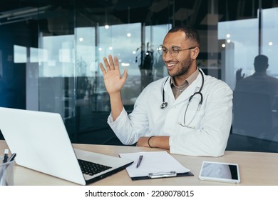 Happy Hispanic Doctor Smiling And Talking On Video Call Man In White Coat And Stethoscope Using Laptop For Remote Online Consultation Smiling And Waving Hello