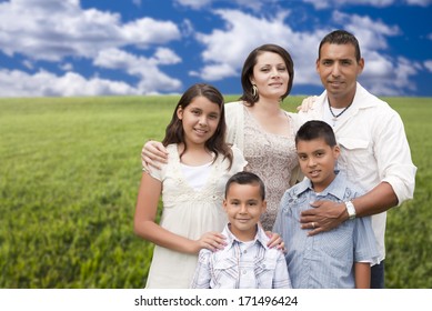 Happy Hispanic Family Portrait Standing In Grass Field.