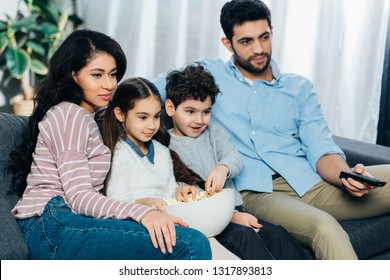 Happy Hispanic Family Watching Tv With Popcorn Bowl At Home