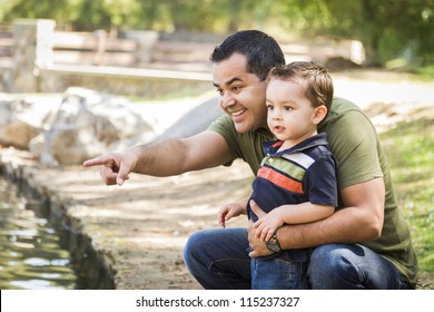 Happy Hispanic Father Points with Mixed Race Son at the Park Pond.