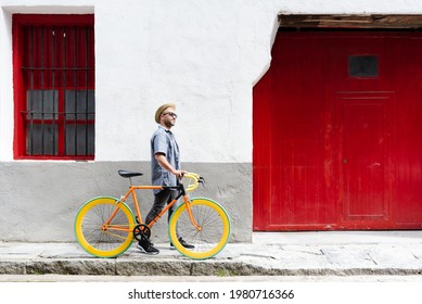 Happy Hispanic Man Carrying A Vintage Bicycle At The Old Town Of A City. Sustainable Tourism Concept.