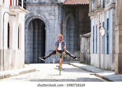 Happy hispanic man riding a bike at the old town of a city, in a cobbled floor street.