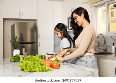 Happy Hispanic mother and daughter preparing fresh vegetables together in a modern kitchen. Family bonding and healthy eating at home. - Powered by Shutterstock