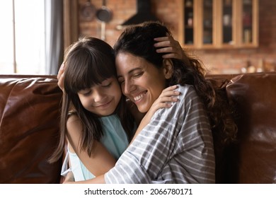 Happy Hispanic Mother Enjoying Time With Beloved Daughter At Home, Hugging Cuddling Girl On Couch, Smiling With Closed Eyes, Feeling Love, Tenderness. Parenthood, Adoption, Motherhood Concept