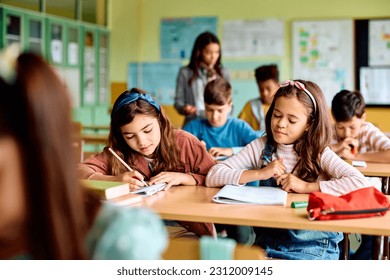 Happy Hispanic schoolgirl and her classmates writing during a class at elementary school.  - Powered by Shutterstock