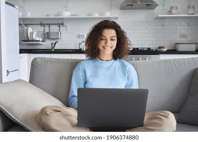 Happy hispanic teen girl holding laptop computer device technology sitting on couch at home. Smiling young woman using apps, searching online, e learning, studying browsing internet on sofa.