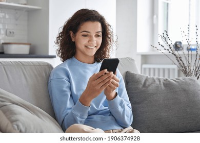 Happy hispanic teen girl holding cell phone using smartphone device at home. Smiling young latin woman blogger subscribing new social media, buying in internet, ordering products online in apps. - Shutterstock ID 1906374928