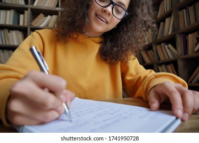 Happy Hispanic Teen Girl School Or College Student Writing In Workbook Doing Homework Or Preparing For Exam In Library Sitting At Desk. Learning Math And Individual Schoolwork Concept, Close Up View.