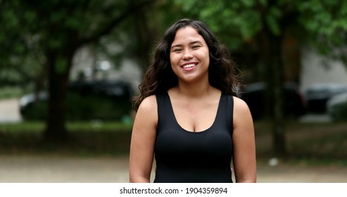 Happy hispanic woman standing outside at park smiling at camera. Mixed race latina girl portrait face, casual real people series