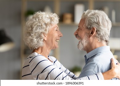 Happy hoary middle aged woman cuddling affectionate senior husband, missing glad to see after long separation. Smiling old mature family couple showing tender sweet feelings to each other at home.