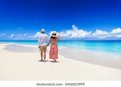 Happy holiday couple with sunhats walks down a tropical paradise beach with turquoise sea and golden sand - Powered by Shutterstock