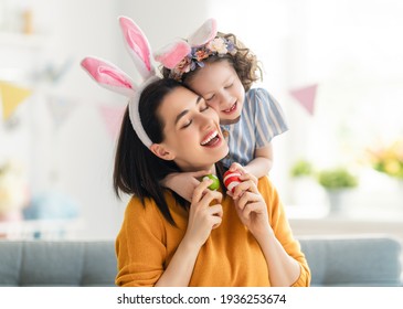 Happy holiday! Mother and her daughter with painting eggs. Family celebrating Easter. Cute little child girl is wearing bunny ears. 