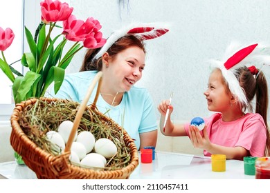 Happy Holiday! Mother And Her Daughter With Painting Eggs. Family Preparing For Easter. Cute Little Child Girl Is Wearing Bunny Ears. An Overweight Mom Smiles At A Girl And Looks At Each Other