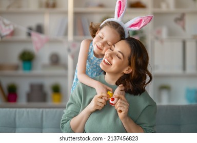 Happy holiday! Mother   her daughter and painting eggs  Family celebrating Easter  Cute little child girl is wearing bunny ears 