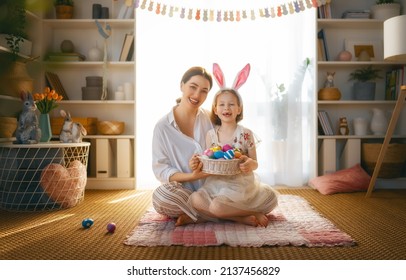 Happy Holiday! Mother And Her Daughter With Painting Eggs. Family Celebrating Easter. Cute Little Child Girl Is Wearing Bunny Ears.