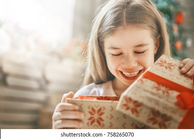 Happy Holidays! Cute Little Child Opening Gift At Christmas.