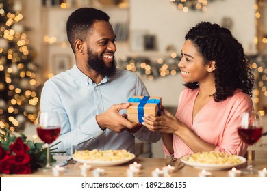 Happy Holidays. Portrait of young black lovers exchanging gifts on anniversary, St Valentine's day or birthday. Smiling couple having romantic dinner and holding present box with blue ribbon