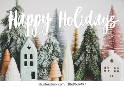 Happy Holidays Text Handwritten On Christmas Little Houses And Trees On White Background,  Winter Cozy Village Scene. Greeting Card, Modern Seasons Greetings