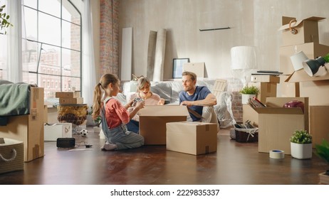 Happy Homeowners Moving In: Lovely Couple Sitting on the Floor of Cozy Apartment Unpacking Cardboard Boxes, Little Daughter Joins them. Cheerful Day, Harmony, Happiness, Sweet Home for Young Family - Powered by Shutterstock