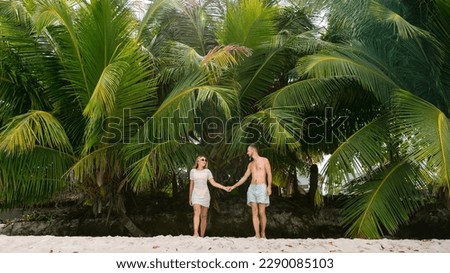 A happy honeymoon couple walks in island against the background of palms.