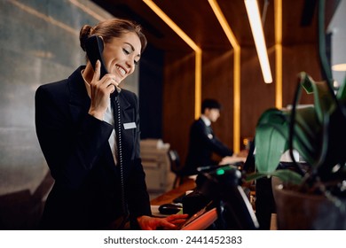 Happy hotel manager talking on the phone at reception desk. - Powered by Shutterstock