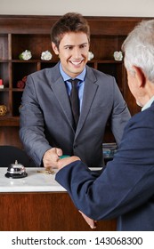 Happy Hotel Receptionist Giving Key Card To Senior Man